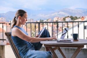 Junge Frau arbeitet auf dem Balkon ihres Appartements-Sie ist Ausgeglichen hat ihre Work-Life-Balance gefunden.
