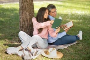 Paar sitzt verliebt in einem Park. Unter einem Baum lesen sie sich gegenseitig vor. Beziehungskrise lösen durch Gemeinsamkeit