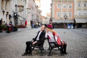 Ein junges Paar sitzt Rücken an Rücken auf zwei Bänken. Auf einem Marktplatz einer Holländischen Stadt. Sie genießen die Qualitätszeit in die Beziehung zu schaffen, durch bewussten liebevollen Umgang trotz des Alltags der die zwei beschäftigt.