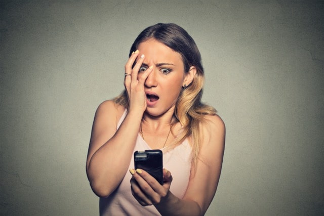 Frau schaut erschrocken auf ihr Smartphone – negative Kommentare in sozialen Medien